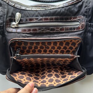 May include: A black nylon handbag with a brown crocodile embossed leather trim. The bag has multiple zippered compartments and a patterned fabric lining.