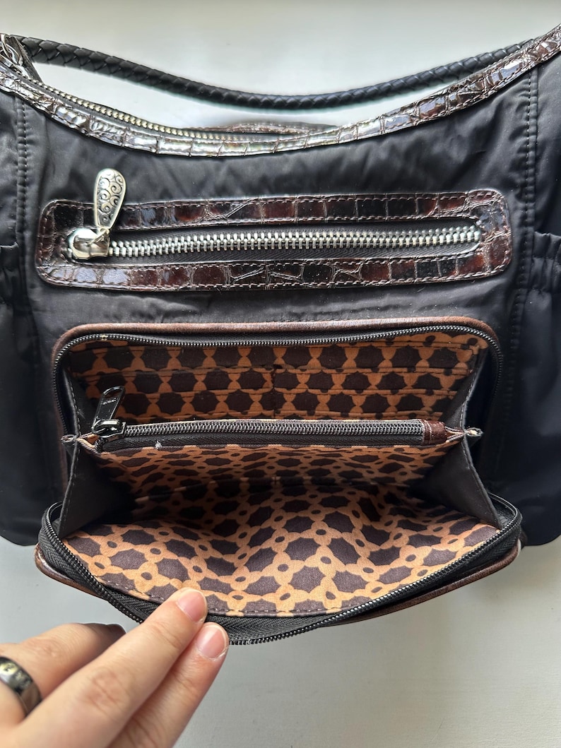 May include: A black nylon handbag with a brown crocodile embossed leather trim. The bag has multiple zippered compartments and a patterned fabric lining.