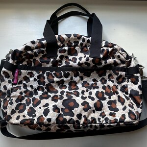 May include: A black and brown leopard print travel bag with a black shoulder strap and a pink zipper pull.
