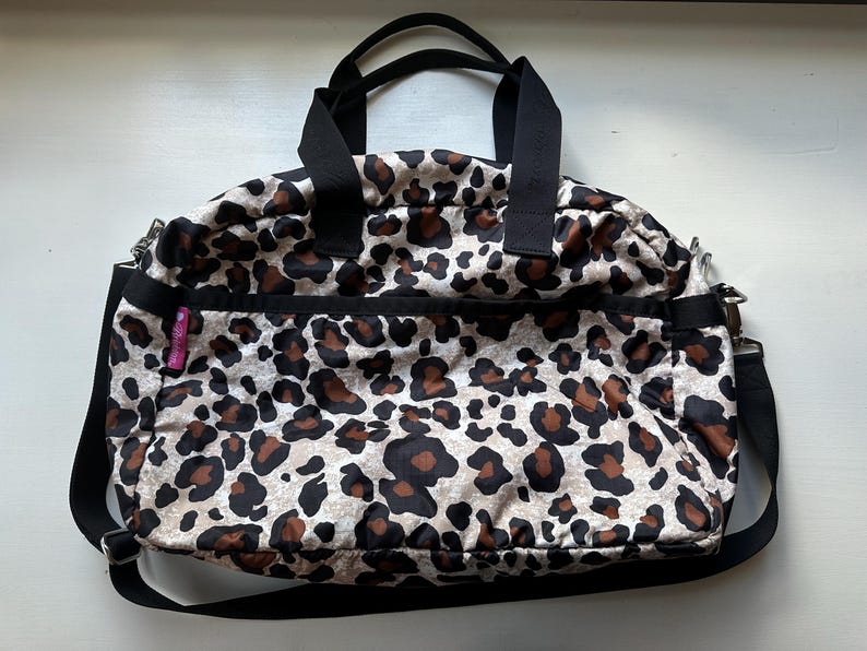 May include: A black and brown leopard print travel bag with a black shoulder strap and a pink zipper pull.