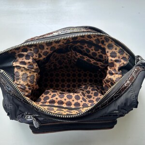 May include: A black and brown handbag with a geometric patterned lining. The bag has a zipper closure and a top handle.