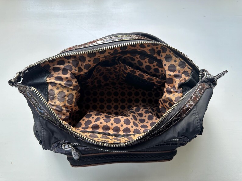 May include: A black and brown handbag with a geometric patterned lining. The bag has a zipper closure and a top handle.