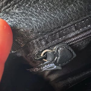 K&ouml;nnte beinhalten: Nahaufnahme eines schwarzen Leder-Rei&szlig;verschlussziehers mit einem silbernen Metall-Schieber. Der Rei&szlig;verschlusszieher hat eine schwarze Lederlasche mit dem eingepr&auml;gten Wort "Brighton".