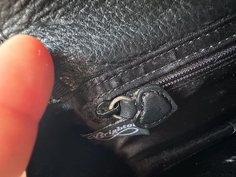 K&ouml;nnte beinhalten: Nahaufnahme eines schwarzen Leder-Rei&szlig;verschlussziehers mit einem silbernen Metall-Schieber. Der Rei&szlig;verschlusszieher hat eine schwarze Lederlasche mit dem eingepr&auml;gten Wort "Brighton".