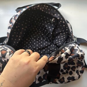 May include: A black and brown leopard print backpack with a black polka dot lining. The backpack is open and the lining is visible.