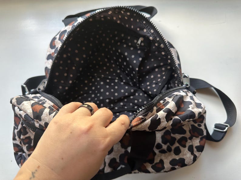 May include: A black and brown leopard print backpack with a black polka dot lining. The backpack is open and the lining is visible.