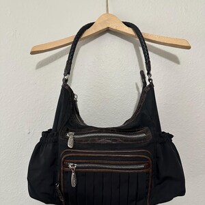 May include: Black nylon handbag with brown leather accents and multiple zippered compartments. The bag has a braided leather strap.