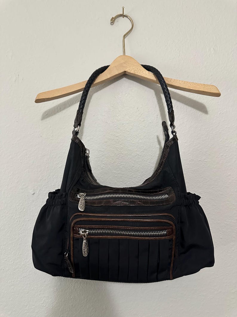 May include: Black nylon handbag with brown leather accents and multiple zippered compartments. The bag has a braided leather strap.