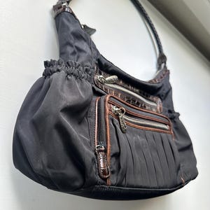 May include: A black nylon handbag with brown leather accents and a zipper closure. The bag has a top handle and a gathered design.