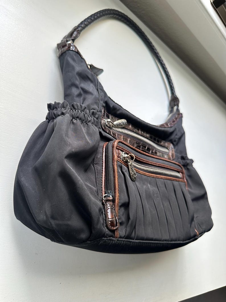 May include: A black nylon handbag with brown leather accents and a zipper closure. The bag has a top handle and a gathered design.