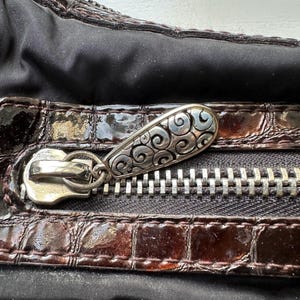 May include: Close-up of a brown leather purse with a silver zipper and a decorative silver pull. The pull has a swirling design.