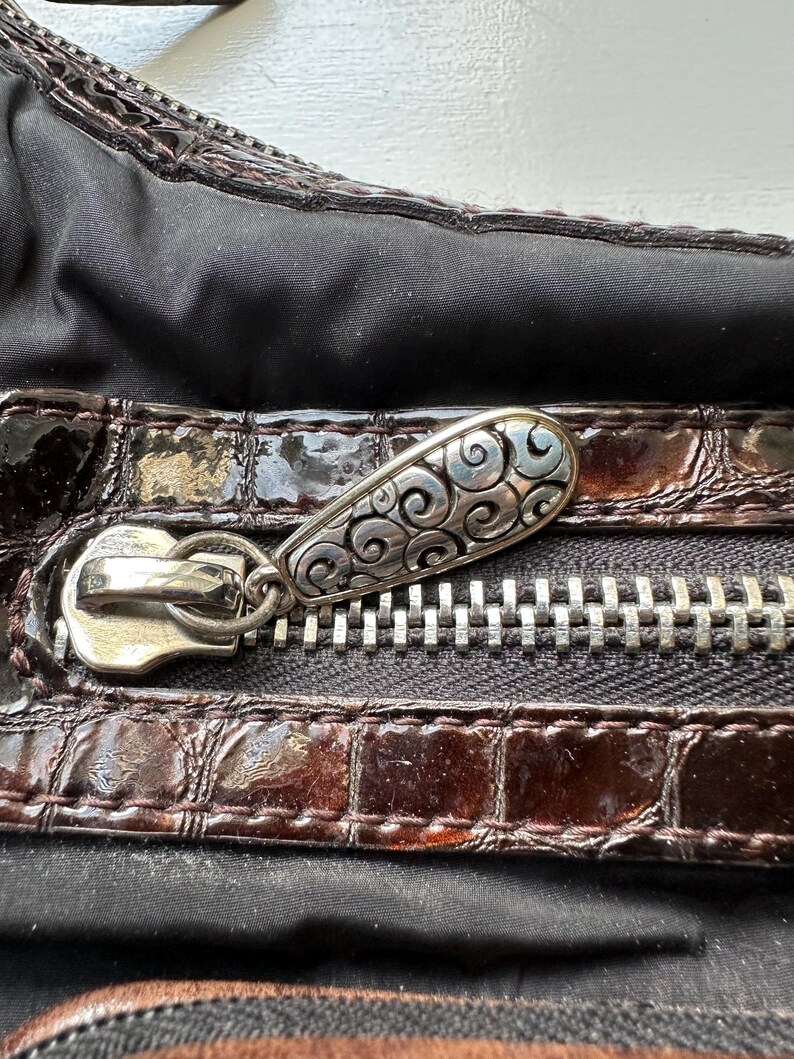 May include: Close-up of a brown leather purse with a silver zipper and a decorative silver pull. The pull has a swirling design.