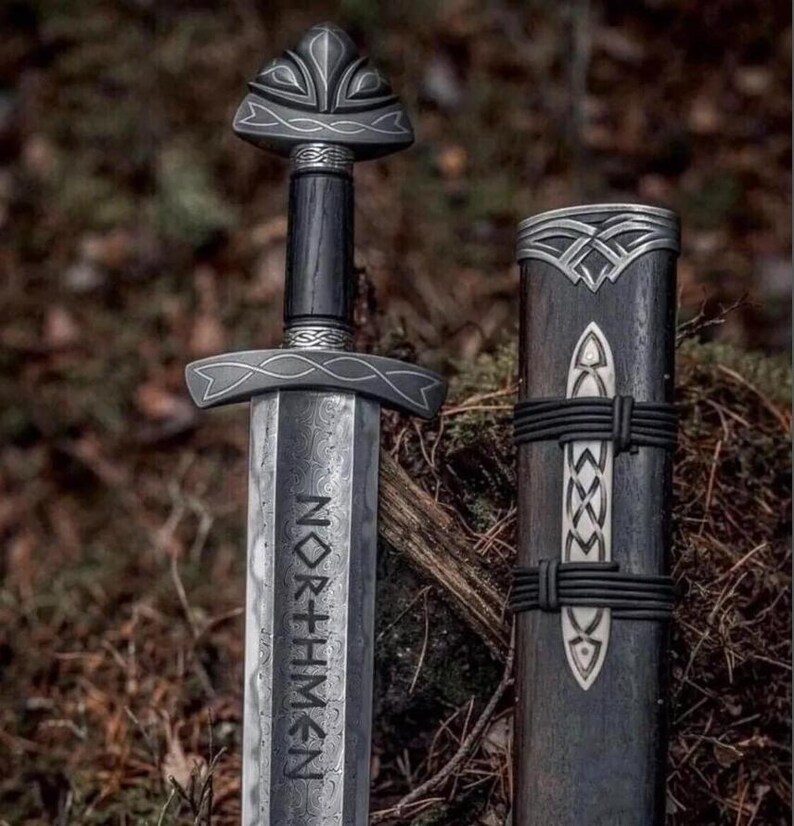 May include: A detailed image of a Viking sword with a dark wooden handle and a silver blade. The blade has the word "NORTHMEN" etched into it. The sword is next to its sheath, which is also dark wood with silver accents.