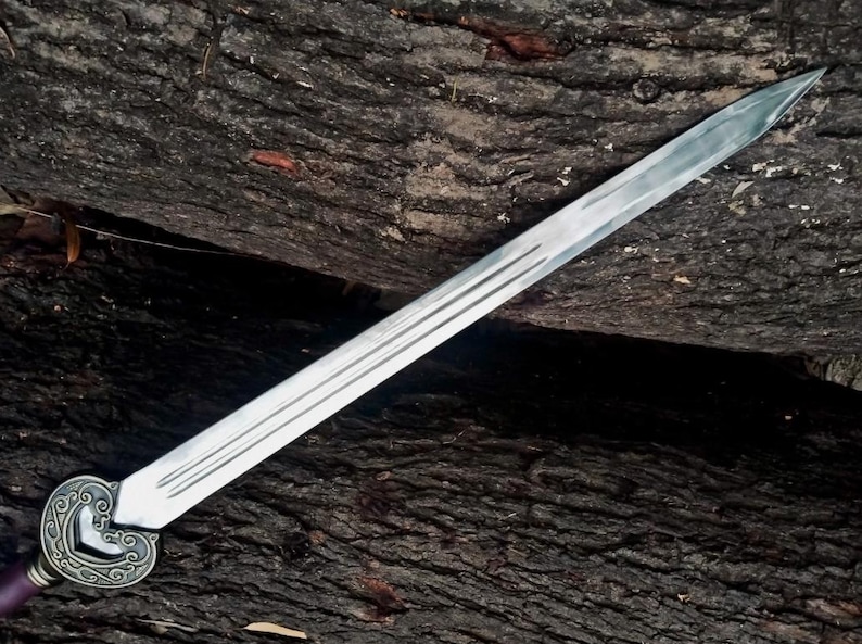 May include: A long, silver sword with a decorative handle and a purple grip. The blade has three parallel grooves running along its length. The sword is set against a dark, textured wooden background.