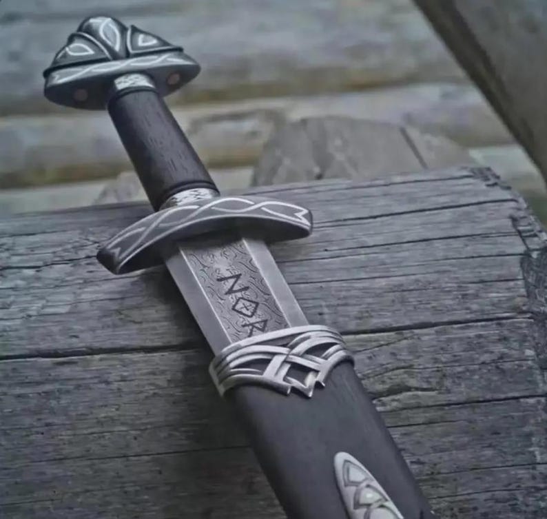 May include: A detailed image of a Viking sword with a dark wooden handle and a silver-colored guard. The blade has etched markings. The sword rests on a weathered wooden surface, showcasing its intricate design and craftsmanship.
