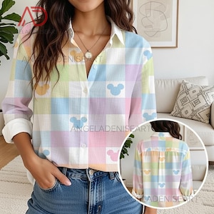 May include: A pastel plaid button-down shirt with white cuffs and collar. The shirt features a pattern of Mickey Mouse silhouettes in blue, yellow, and pink. The text "ANGELADENISEART" is visible on the shirt.