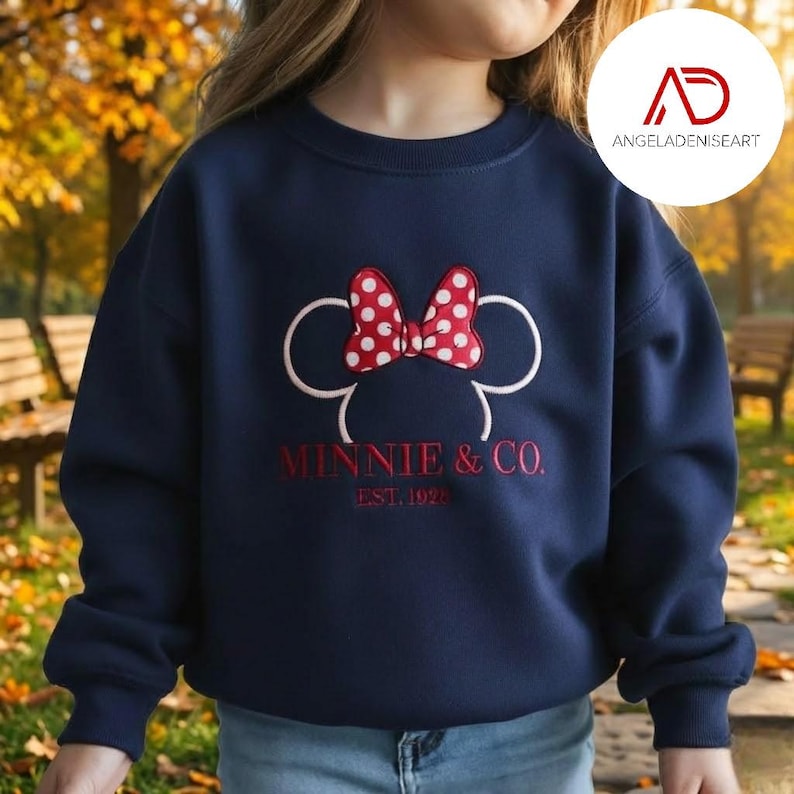A person wearing a navy blue sweatshirt with a red and white polka dot Minnie Mouse design and the text "MINNIE & CO. EST. 1920" printed on it.