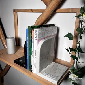 May include: A pair of marble bookends, one black and one white, holding cookbooks on a wooden shelf. The white bookend has the word "lehome" on it. A white candle and decorative branches are also visible.