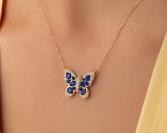 Op de afbeelding: Een gouden ketting met een vlindervormige hanger. De vlindervleugels zijn ingelegd met diepblauwe, peervormige stenen en omlijnd met kleine, heldere, fonkelende steentjes. De hanger hangt aan een delicate, dunne gouden ketting.
