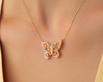 Op de afbeelding: Een gouden ketting met een vlinderhanger. De vleugels van de vlinder zijn versierd met kleine oranje steentjes en piepkleine doorzichtige accentsteentjes langs de randen. De hanger hangt aan een fijne gouden schakelketting om de hals.