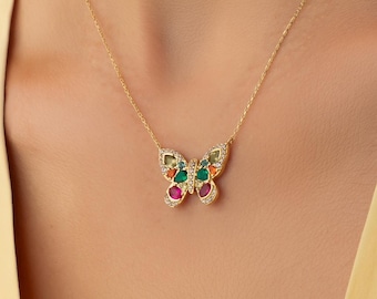 Op de afbeelding: Een gouden ketting met een vlindervormige hanger. De hanger is aan de randen bezet met kleine heldere steentjes en bevat ingelegde druppelvormige stenen in levendige tinten rood, groen, oranje en blauw.