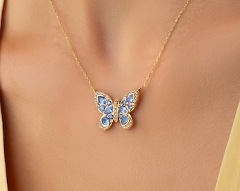 Op de afbeelding: Een gouden ketting met een vlinderhanger. De vleugels van de vlinder zijn ingelegd met lichtblauwe stenen en geaccentueerd met kleine heldere steentjes langs de randen. De hanger hangt aan een fijne gouden schakelketting.