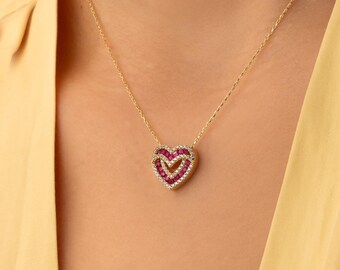 Op de afbeelding: Een gouden ketting met een hartvormige hanger. De hanger bestaat uit een centraal hart gevuld met kleine rode steentjes, omringd door een rand van piepkleine doorzichtige steentjes, gevat in een gouden frame dat bij de ketting past.
