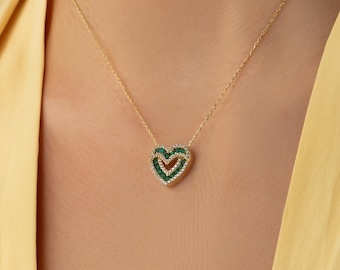 Op de afbeelding: Een gouden ketting met een hartvormige hanger. De hanger bestaat uit een binnenste laag van kleine groene steentjes omringd door een buitenste rand van heldere witte steentjes, wat zorgt voor een gelaagd hartontwerp aan een fijne ketting.
