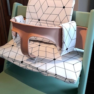 May include: A high chair with a light green frame and a peach-colored safety bar. The seat and backrest feature a white fabric with a black geometric pattern. The chair is designed for infants and toddlers.