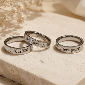 May include: Three silver-toned metal rings with engraved text. One ring features the date 05.10.2020, another is engraved with the words My Soulmate, and the third ring displays the phrase I love you followed by a small heart symbol.