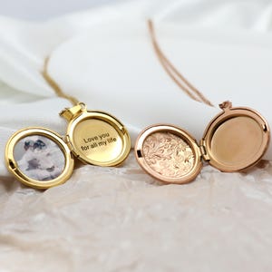 May include: Two open oval lockets on fine chains. One is gold-toned with a photo and the inscription "Love you for all my life." The other is rose gold with an engraved floral design. Both are displayed against a soft, white background.