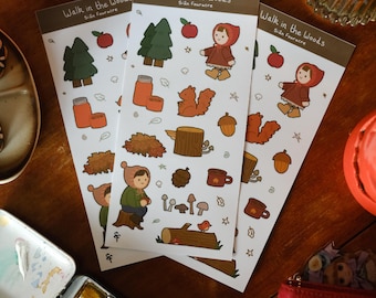 May include: Three sticker sheets with woodland-themed illustrations, including a girl in a red hooded cloak, trees, squirrels, and mushrooms. The text "Walk in the Woods" and the artist's name are at the top. The stickers are on a wooden surface.