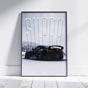 Può includere: Poster con cornice nera con un'auto sportiva nera con spoiler posteriore. La parola "SUPRA" è visualizzata in grandi lettere bianche stilizzate sopra l'auto. Lo sfondo mostra un paesaggio innevato. Il poster è appoggiato a una parete bianca.