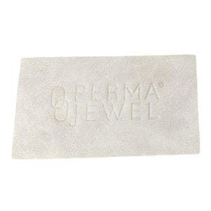 May include: A rectangular, off-white textured surface with the embossed text "PERMA JEWEL". The surface has a subtle, mottled appearance, and the lettering is in a sans-serif font. The overall aesthetic is clean and minimalist.