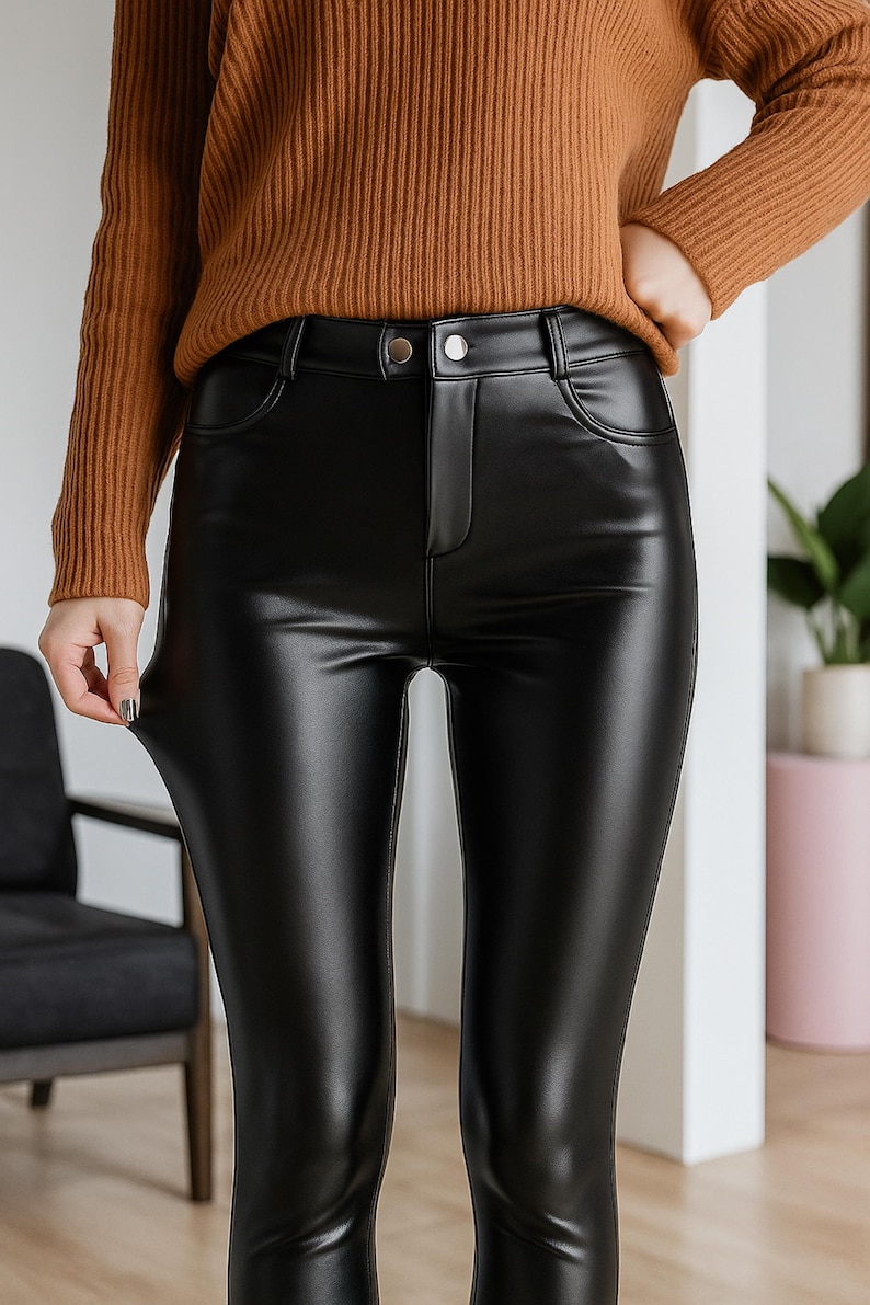 Puede incluir: Pantalones negros de cuero sint&eacute;tico con cintura alta y cierre de bot&oacute;n. Los pantalones tienen un acabado brillante y un dise&ntilde;o cl&aacute;sico de cinco bolsillos. La modelo lleva un su&eacute;ter marr&oacute;n.