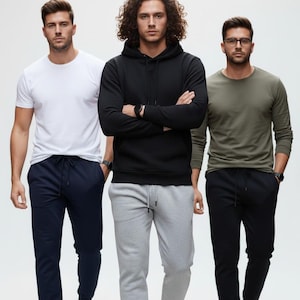 May include: Three people wearing casual clothing, including a white t-shirt, black hoodie, and olive green long-sleeve shirt. They are wearing sweatpants in navy, gray, and black, paired with sneakers. The background is plain white.