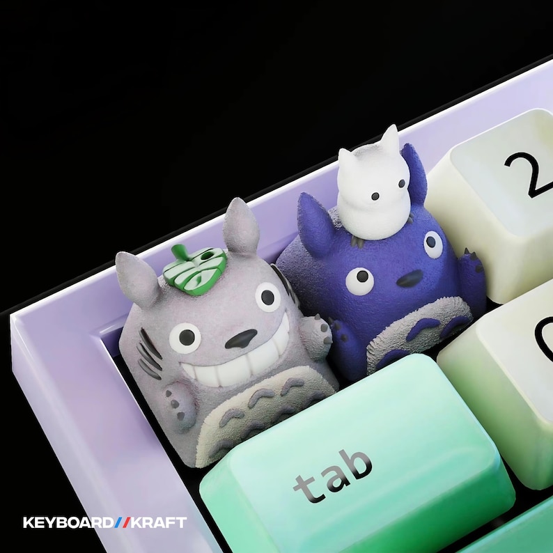 May include: Close-up of a keyboard with custom keycaps featuring cartoon characters. One keycap is light gray with a green leaf, and the other is dark blue with a white figure on top. The "tab" key is light green. The text "KEYBOARD // KRAFT" is visible.