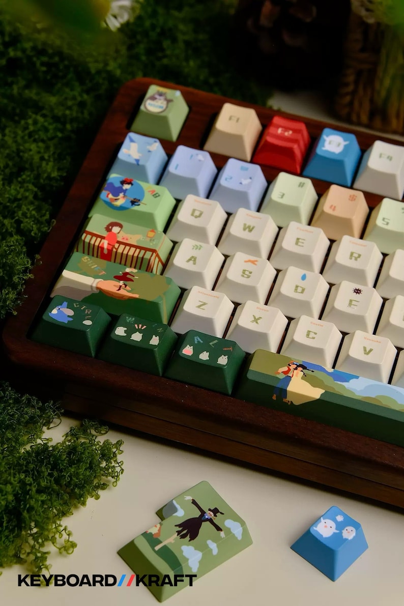 May include: Custom mechanical keyboard with keycaps featuring colorful illustrations. The keycaps have various designs, including cartoon characters and landscapes. The keyboard is set in a dark wood frame, with the text "KEYBOARD//KRAFT" visible.