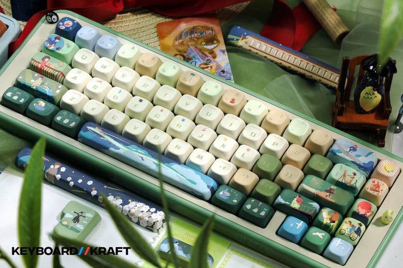 May include: A custom mechanical keyboard with a green frame and keycaps featuring various illustrations. The keycaps have a mix of colors, including white, green, and blue, with images of landscapes and characters. The keyboard has a wrist rest with a blue and white design. The text "KEYBOARD//KRAFT" is visible.