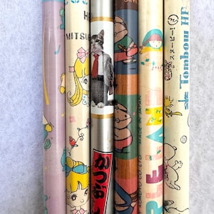 以下が含まれることがあります： カラフルなデザインとイラストが施された、ヴィンテージの鉛筆のコレクション。スーツを着た猫、スヌーピー、その他の漫画のキャラクターなど、さまざまなキャラクターが登場します。鉛筆の色は、ピンク、ブルー、クリームなど様々です。