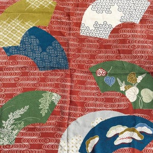 May include: A textile with a red background featuring a repeating pattern of white swirls. Overlaid are several fan-shaped designs in various colors, including green, blue, and white, each with intricate patterns and floral motifs.