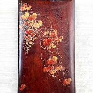 May include: A rectangular, wooden box with a rich, dark brown finish. The surface is adorned with a delicate floral design in shades of red and gold. The design features stylized leaves and vines, creating an elegant, artistic aesthetic.