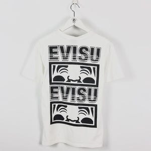 May include: White t-shirt with a black graphic design. The design features the word "EVISU" stacked twice, with a stylized face graphic in between. The shirt has short sleeves and a crew neck.