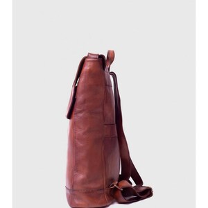 May include: A brown leather backpack with a flap closure and adjustable straps. The backpack has a rectangular shape with visible stitching and a buckle detail. The leather has a rich, textured appearance.