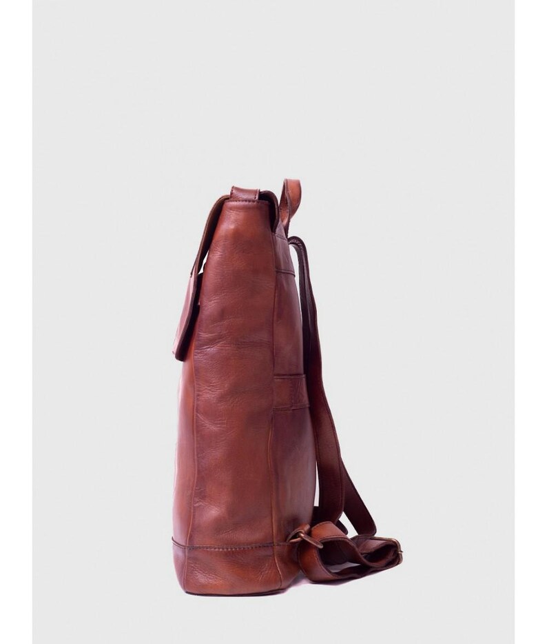 May include: A brown leather backpack with a flap closure and adjustable straps. The backpack has a rectangular shape with visible stitching and a buckle detail. The leather has a rich, textured appearance.