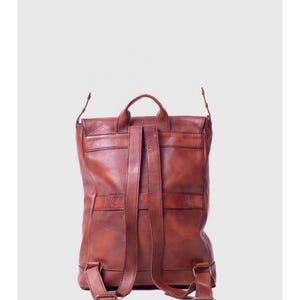May include: A brown leather backpack with adjustable shoulder straps and a top handle. The backpack has a flap closure and multiple pockets. The leather has a distressed look.