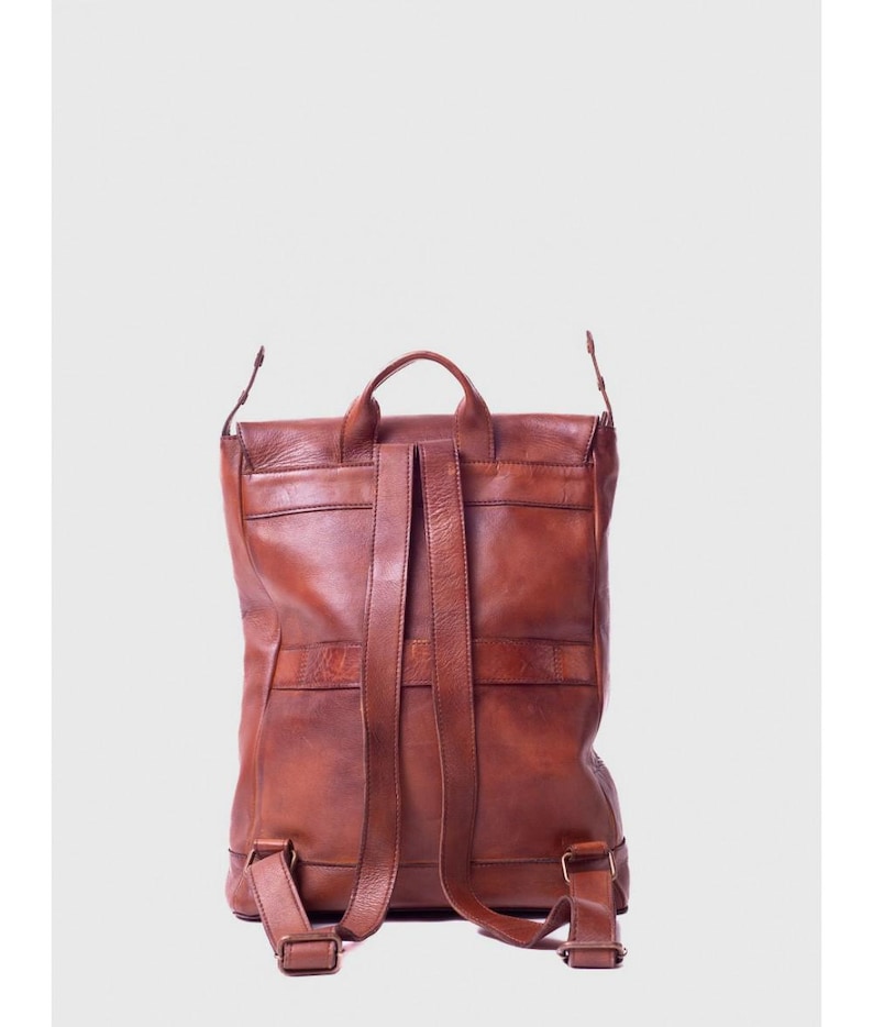 May include: A brown leather backpack with adjustable shoulder straps and a top handle. The backpack has a flap closure and multiple pockets. The leather has a distressed look.