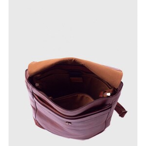 May include: Open brown leather messenger bag with a flap closure. The bag has multiple compartments, including a zippered pocket and a smaller front pocket. The interior is lined with a lighter brown fabric.