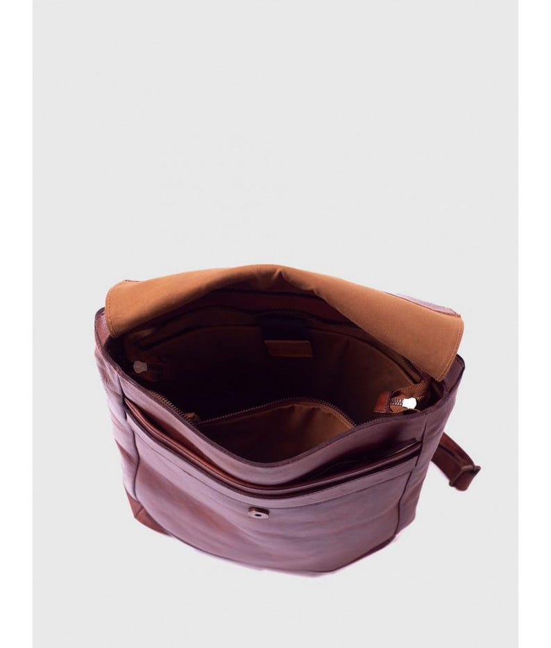 May include: Open brown leather messenger bag with a flap closure. The bag has multiple compartments, including a zippered pocket and a smaller front pocket. The interior is lined with a lighter brown fabric.