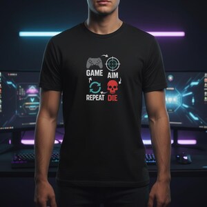Könnte beinhalten: Schwarzes T-Shirt mit einem Gaming-Motiv. Das Design zeigt einen Controller, ein Fadenkreuz, einen Totenkopf und die Worte "GAME AIM REPEAT DIE". Text und Grafiken sind in Weiß und Rot gehalten.